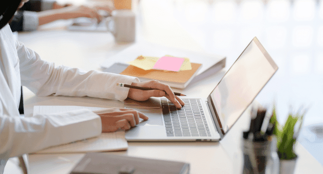Person working on a laptop beside a notebook and colorful sticky notes.